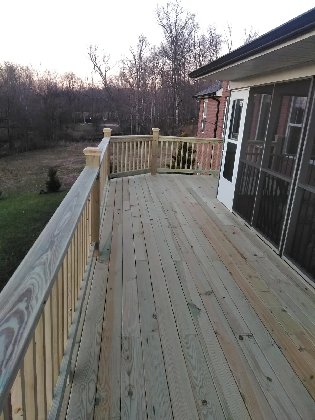 Wooden deck and railing beside a screened porch